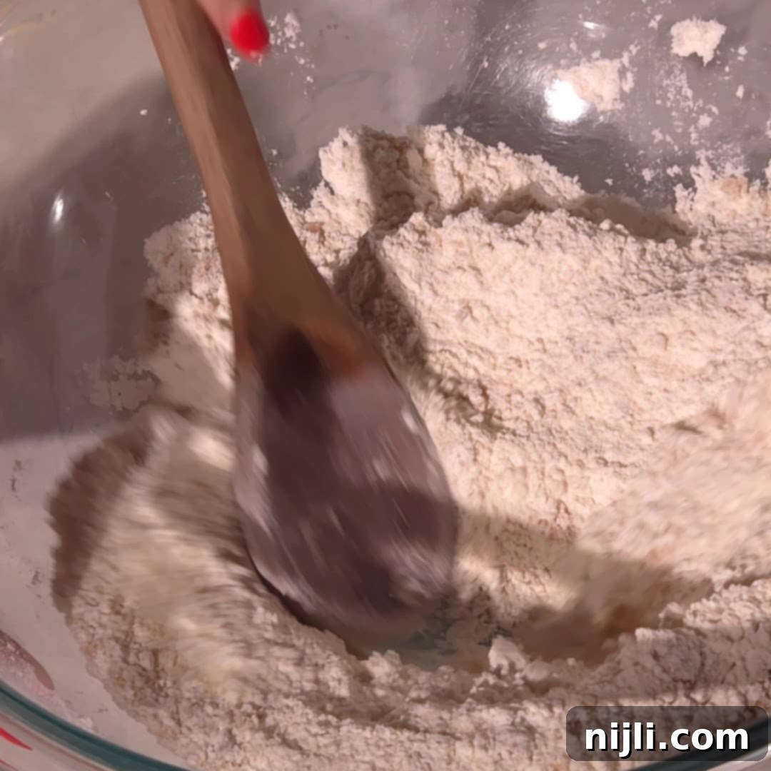 Homemade Blackberry Coffee Cake 8 A wooden spoon stirs flour in a glass bowl to combine dry ingredients for blackberry coffee cake.