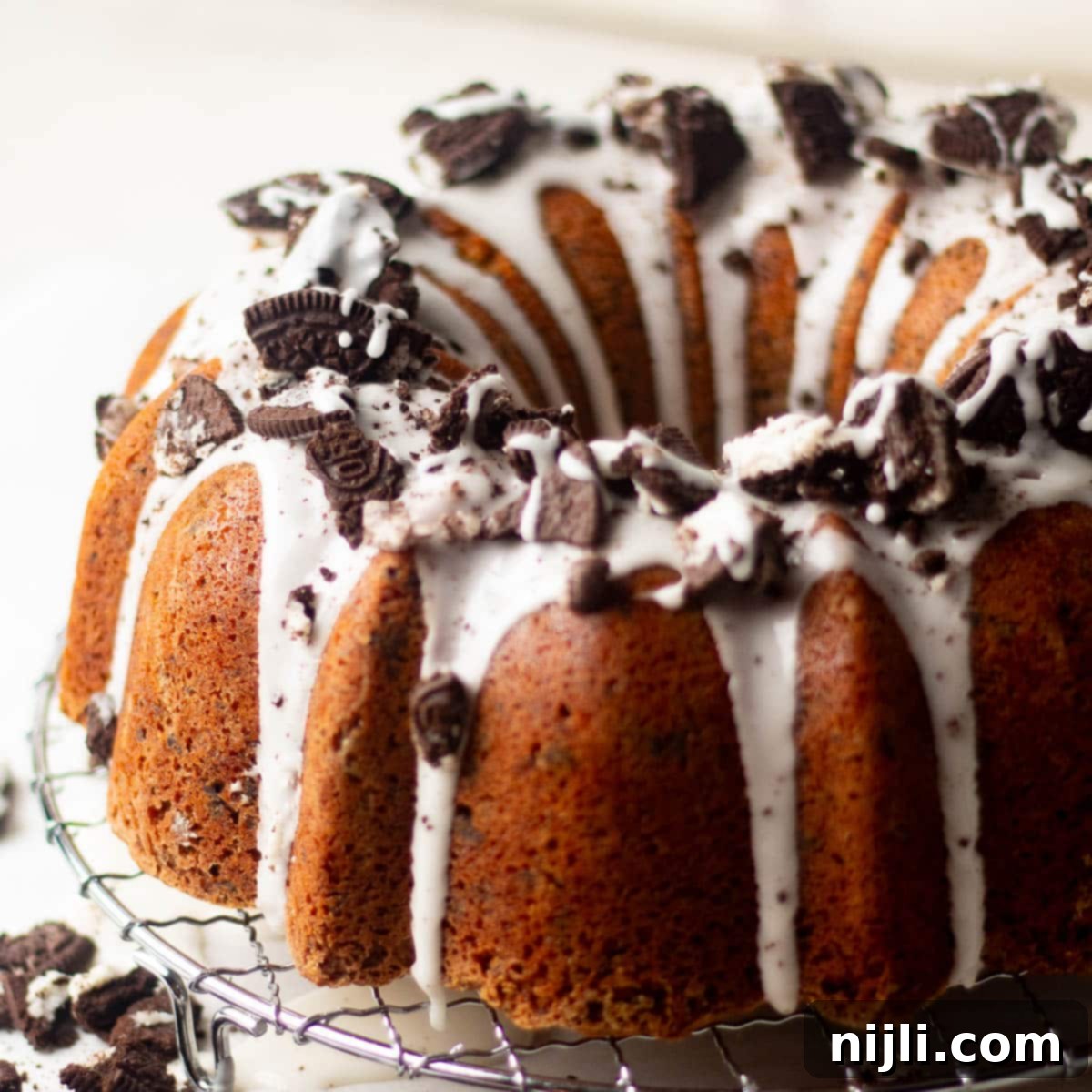 Decadent Oreo Pound Cake 2 Angled close-up of Oreo pound cake showing thick vanilla glaze dripping over the Bundt ridges and loaded with chunks of crushed Oreos.