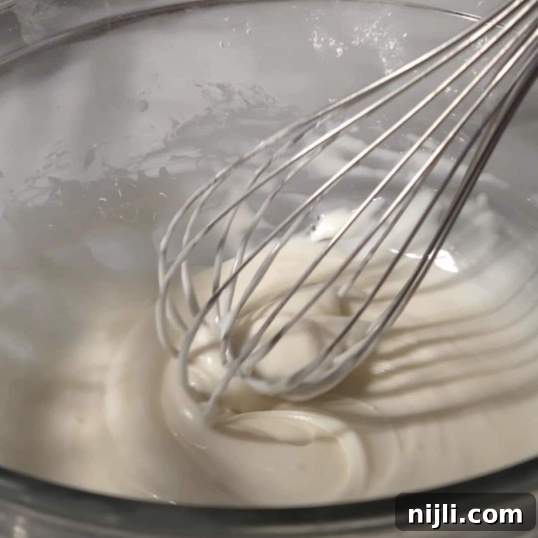 Decadent Oreo Pound Cake 13 A whisk mixing smooth white glaze in a glass bowl, ready to be poured over the Oreo pound cake.