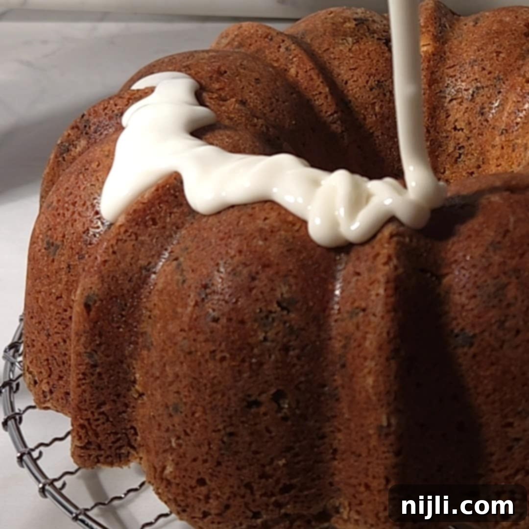 Decadent Oreo Pound Cake 14 Close-up of white glaze being drizzled over the top of a freshly baked Oreo pound cake in a Bundt shape.