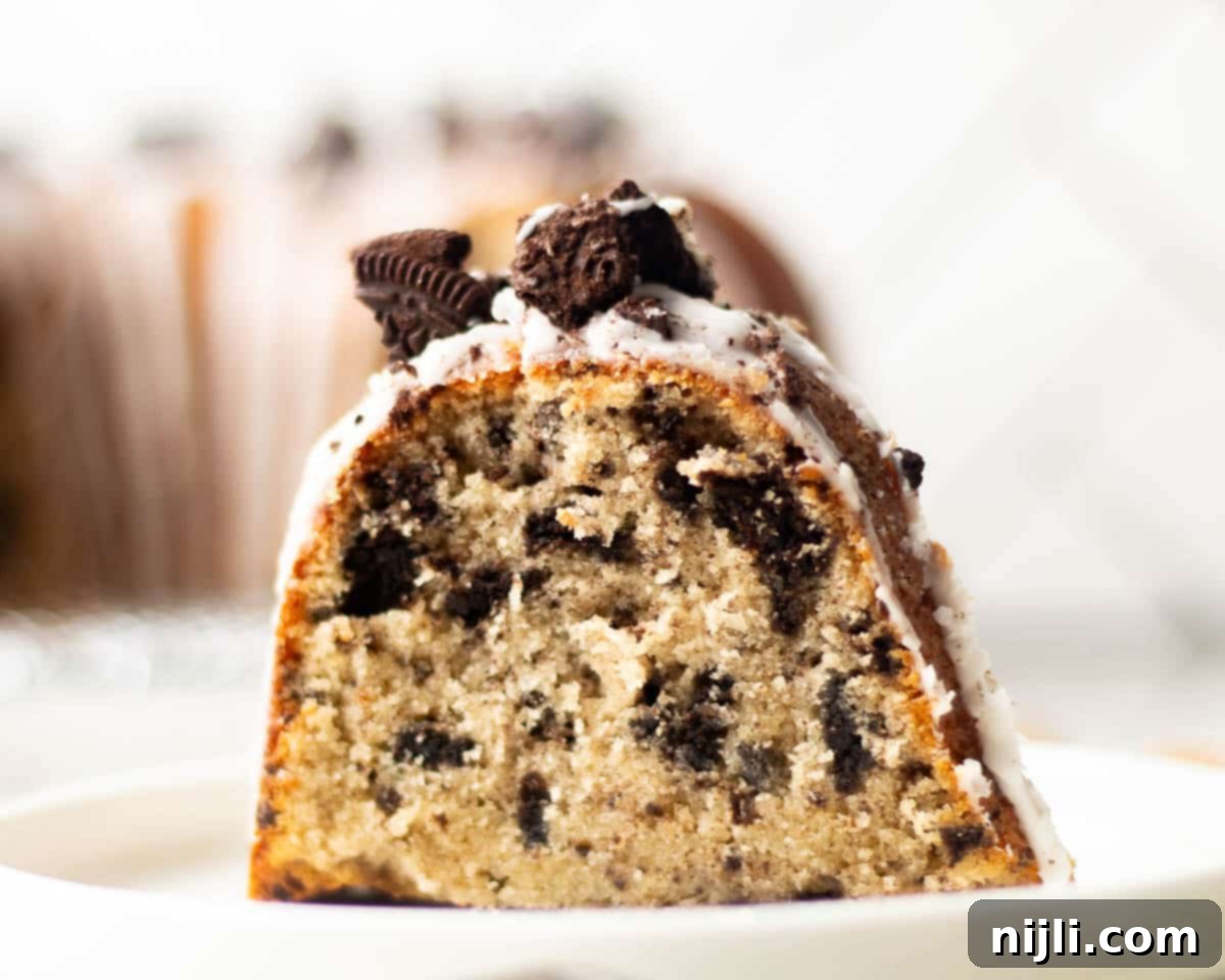 Decadent Oreo Pound Cake 15 A single slice of Oreo pound cake on a white plate, showing a soft, moist crumb filled with crushed Oreos and topped with vanilla glaze and cookie chunks.