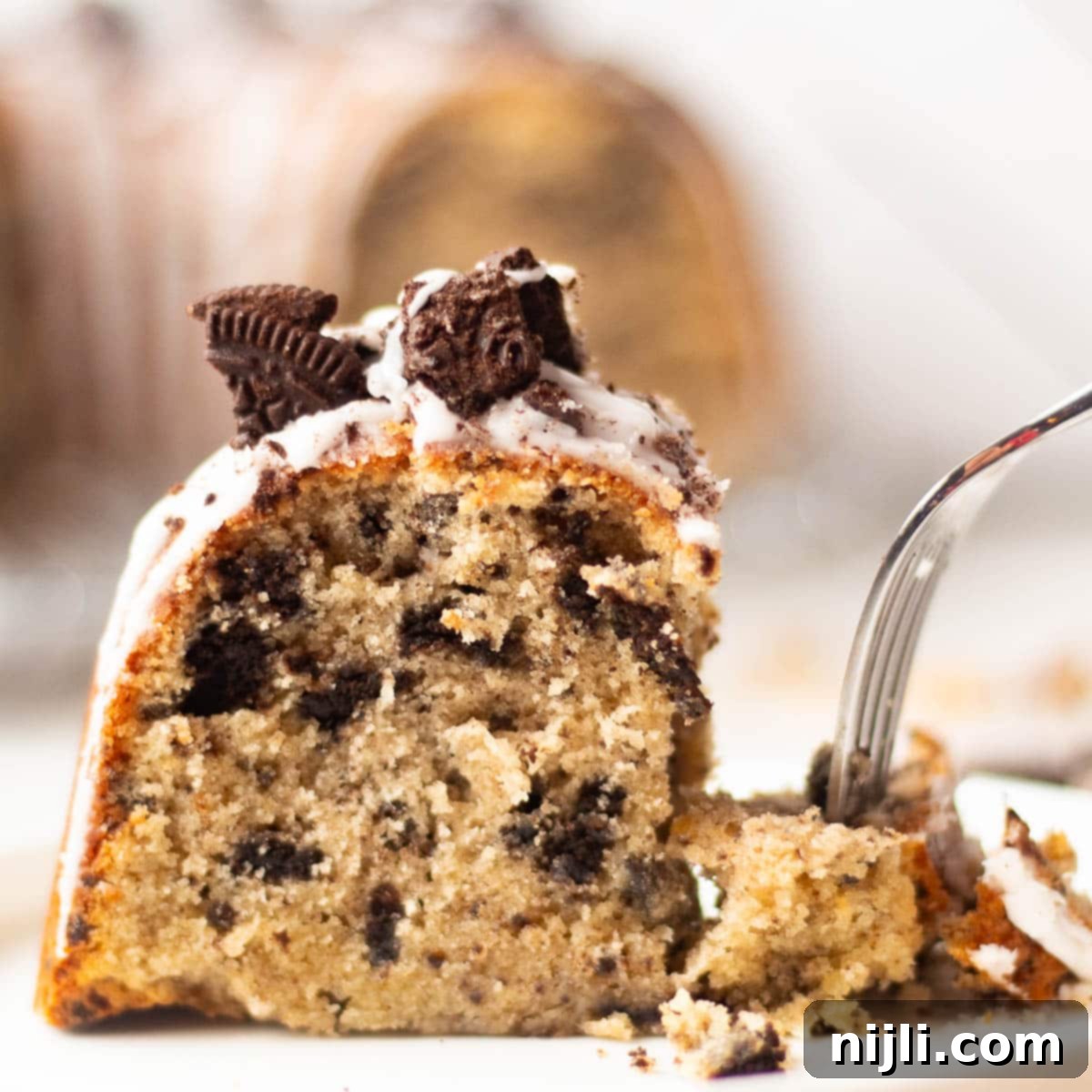 Decadent Oreo Pound Cake 16 A slice of Oreo pound cake on a plate with a bite taken out, revealing a soft, moist texture with crushed Oreos and white icing topped with cookie chunks.