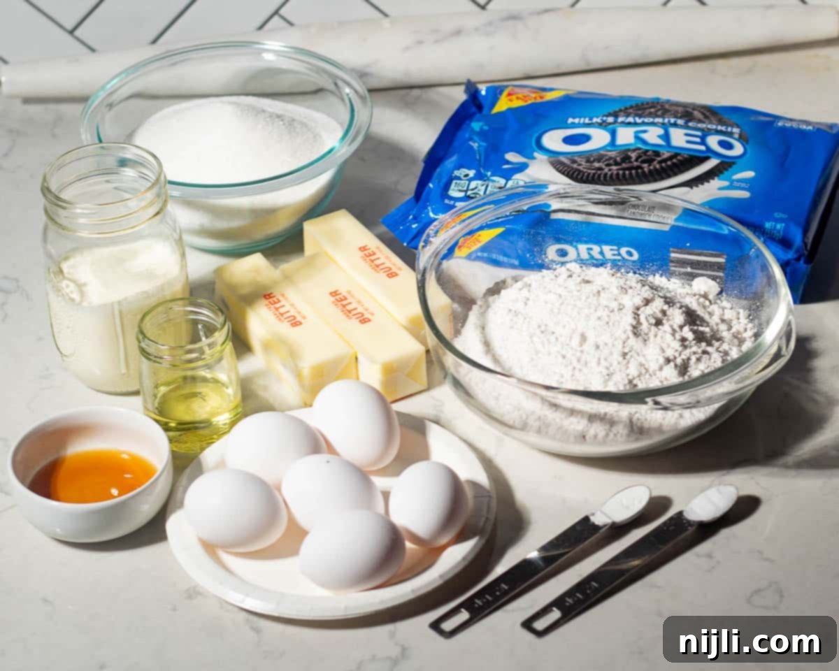 Decadent Oreo Pound Cake 4 Ingredients for Oreo pound cake arranged on a countertop, including flour, sugar, butter, eggs, sour cream, oil, vanilla extract, baking soda, salt, and a package of Oreo cookies.