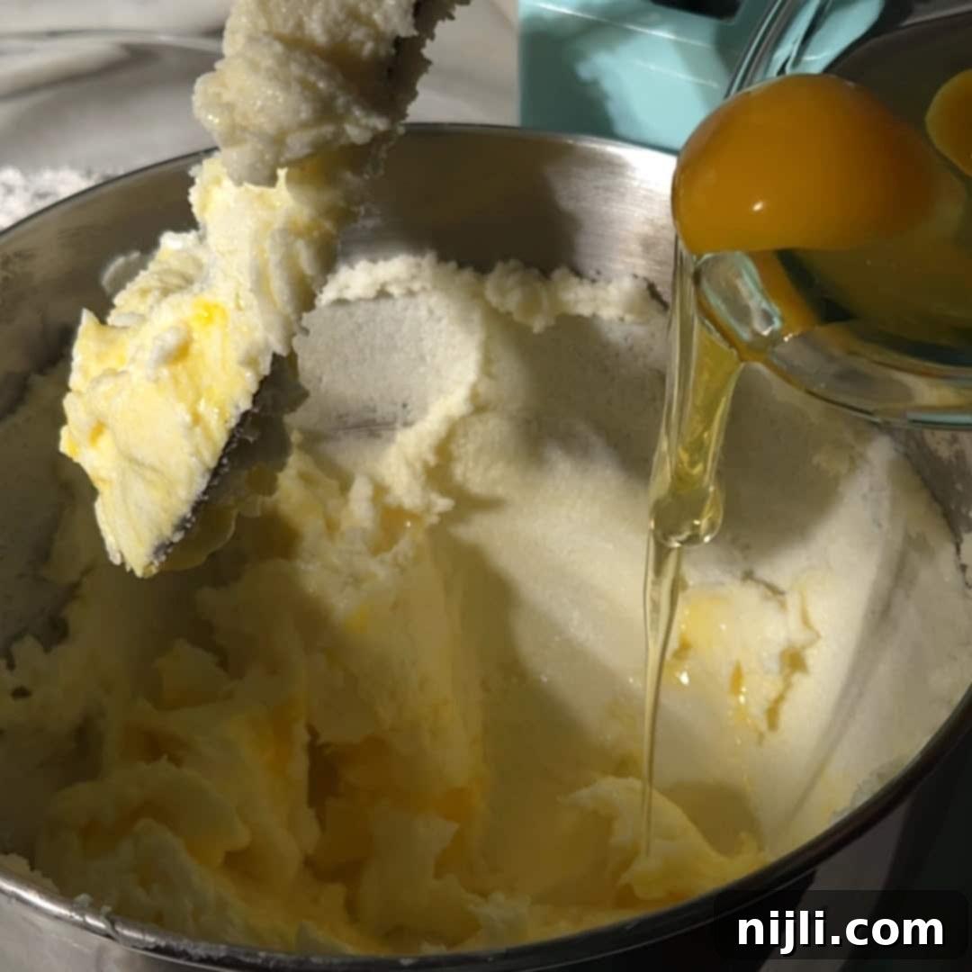 Decadent Oreo Pound Cake 8 Step-by-step shot of Oreo pound cake batter being mixed, with raw eggs being poured into a bowl of creamed butter and sugar.