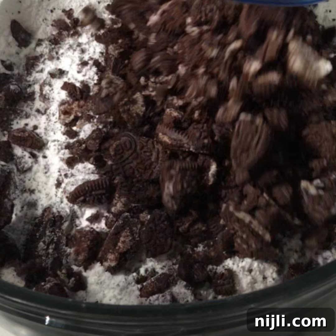 Decadent Oreo Pound Cake 10 Crushed Oreo cookies being folded into flour in a mixing bowl as part of the Oreo pound cake batter prep.