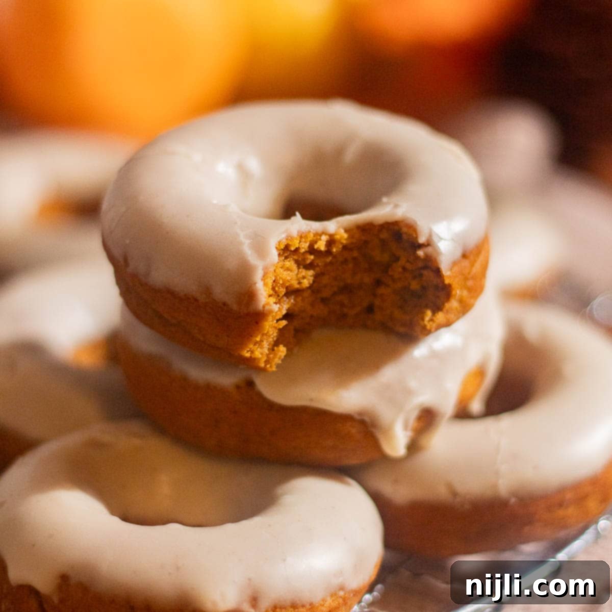 Spiced Pumpkin Perfection 2 Square image of a bitten pumpkin spice donut stacked on others, highlighting its rich, tender crumb and creamy glaze.