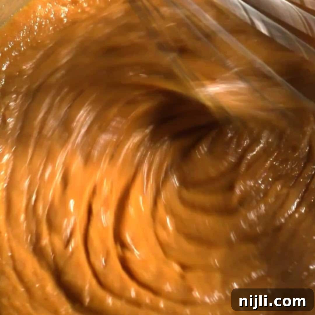 Spiced Pumpkin Perfection 11 Smooth and glossy pumpkin spice donut batter being whisked in a glass bowl with visible swirl motion.
