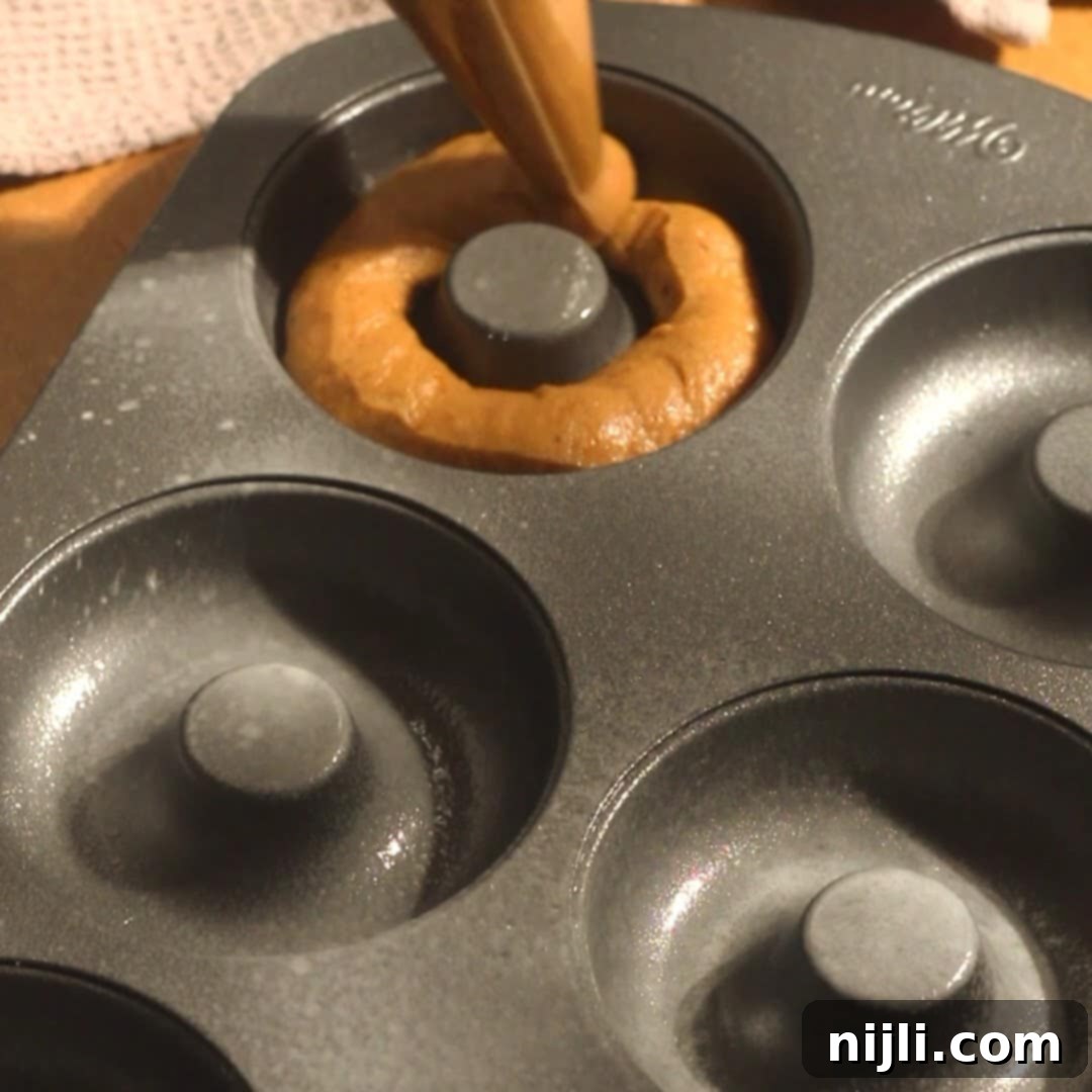 Spiced Pumpkin Perfection 13 Pumpkin spice donuts batter being piped into a greased donut pan cavity, ready for baking.