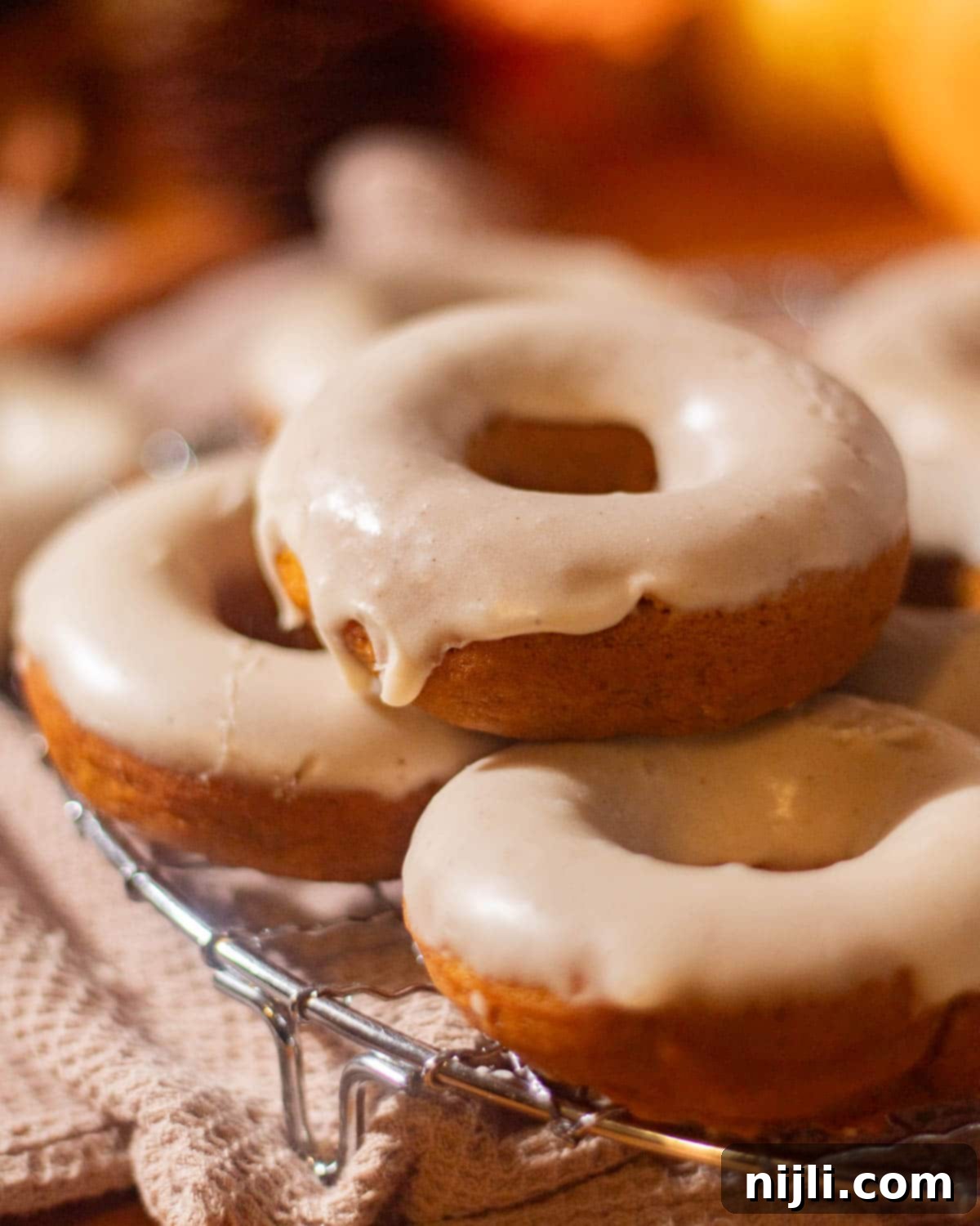 Spiced Pumpkin Perfection 3 A cooling rack filled with warm pumpkin spice donuts, each covered in a thick layer of drippy brown butter glaze, photographed in natural light.