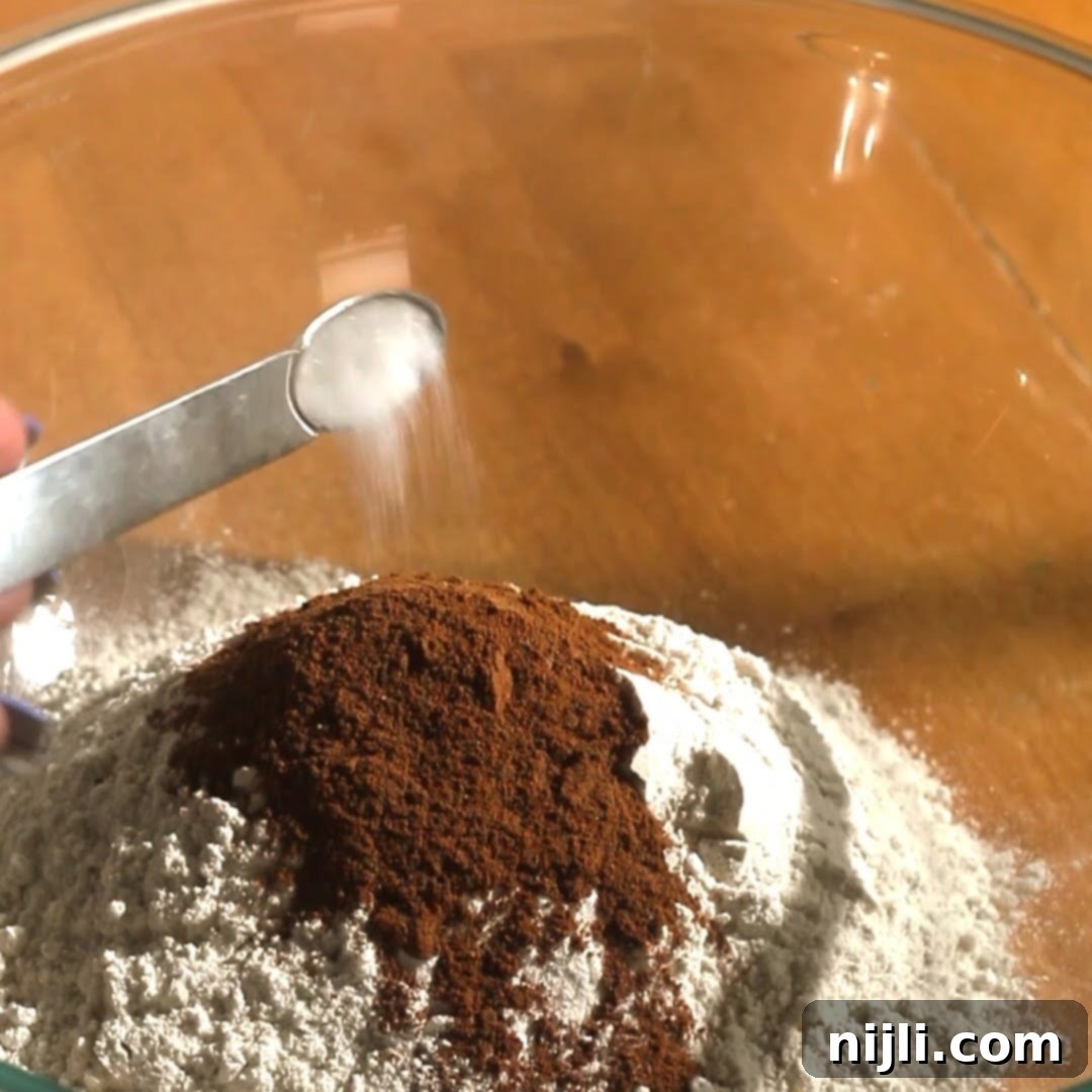 Spiced Pumpkin Perfection 9 Spoonful of salt being added to a bowl of flour and pumpkin pie spices, prepping dry ingredients for pumpkin spice donuts.