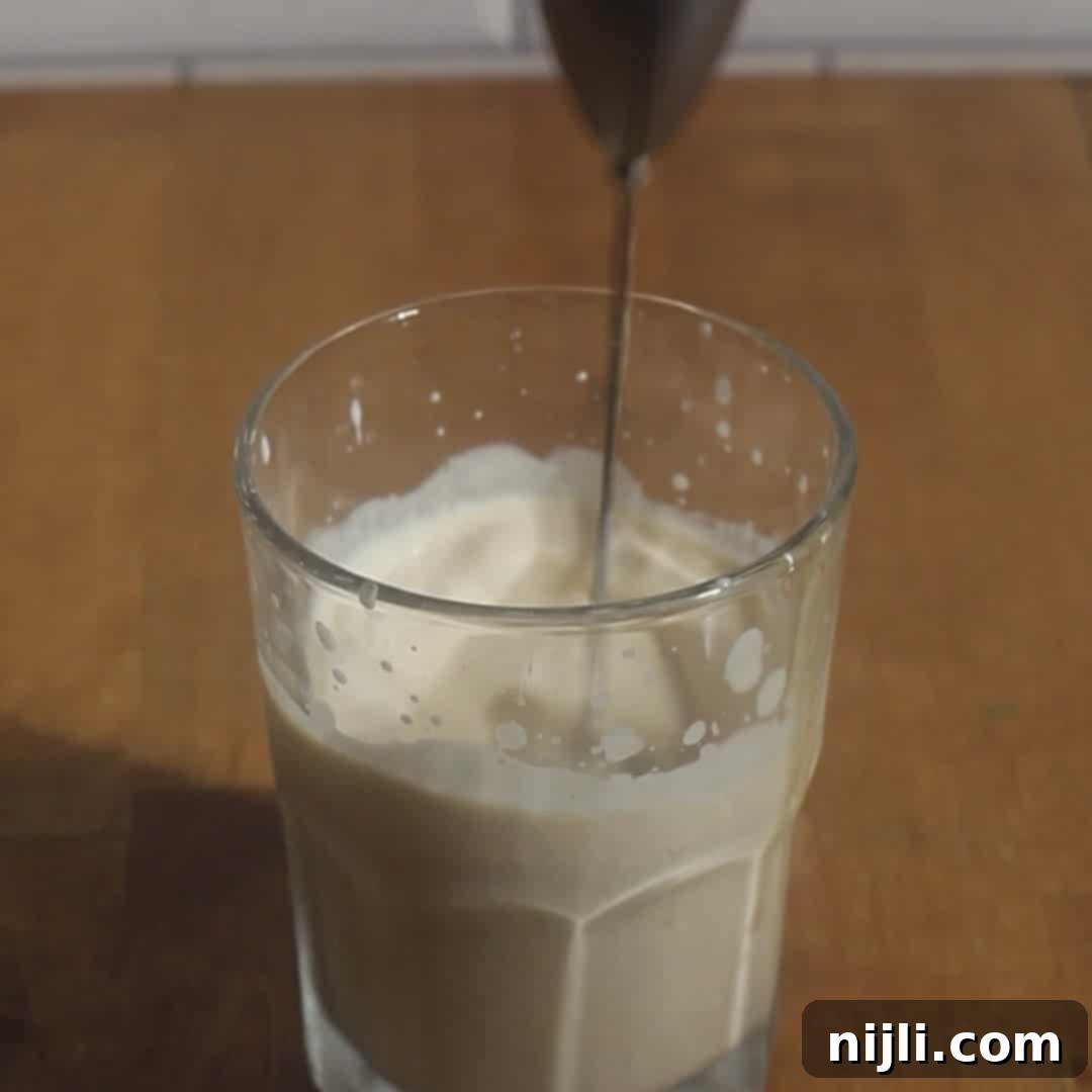 Starbucks Style Pumpkin Cold Foam 11 Hand frothing cream and pumpkin mixture in a glass with a handheld frother to make pumpkin cold foam.