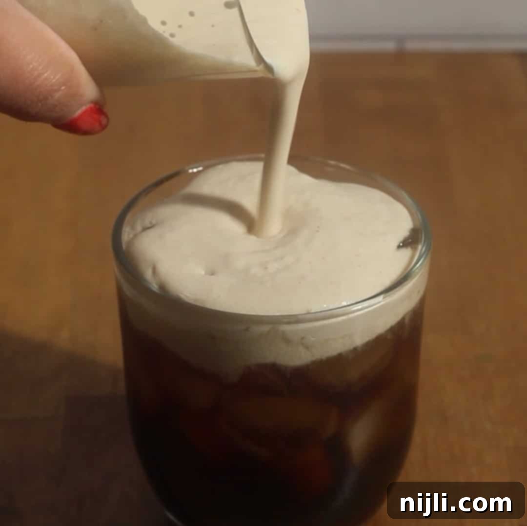 Starbucks Style Pumpkin Cold Foam 12 Pumpkin cold foam being poured over iced coffee in a clear glass.