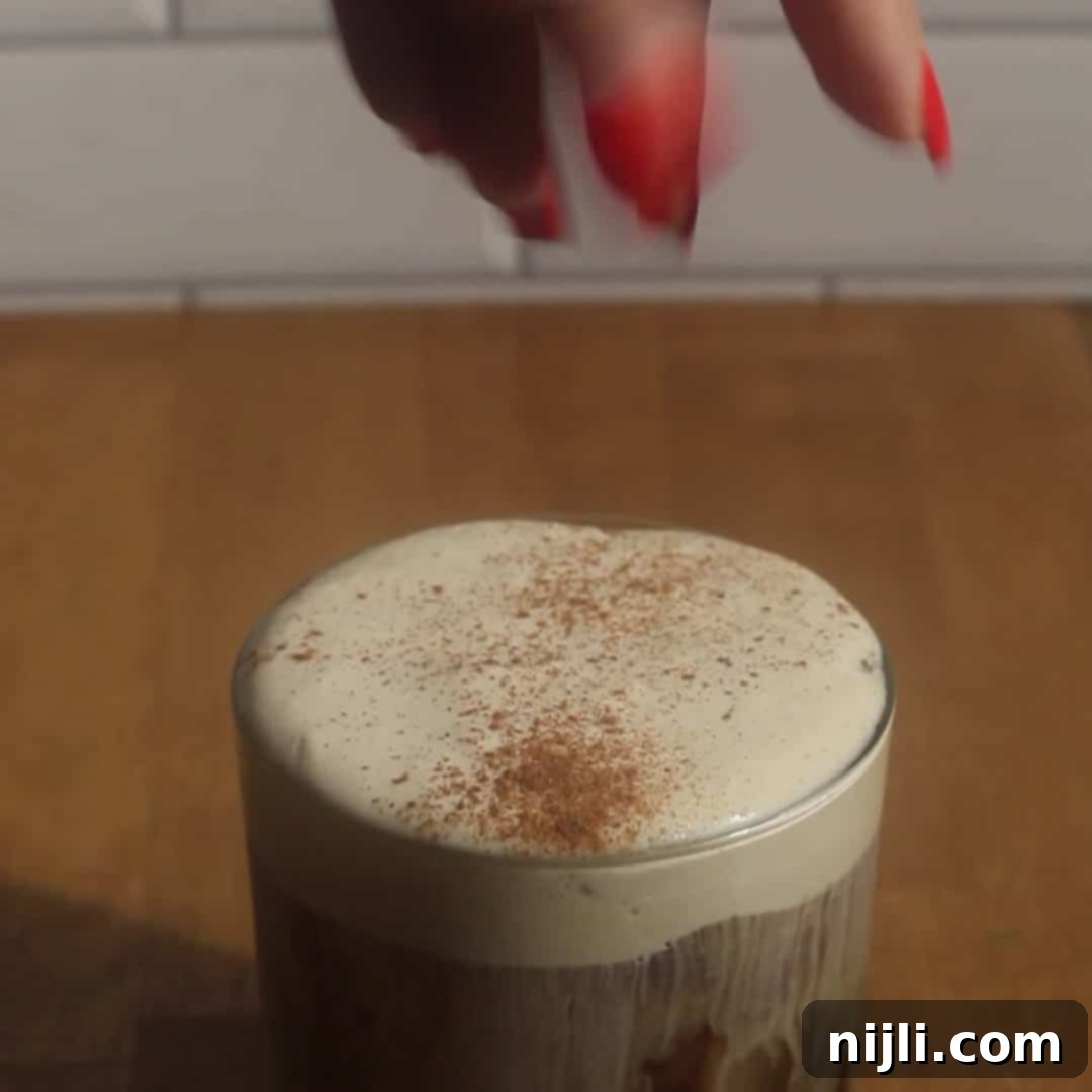 Starbucks Style Pumpkin Cold Foam 13 Glass of iced coffee topped with pumpkin cold foam, hand sprinkling cinnamon spice on top.