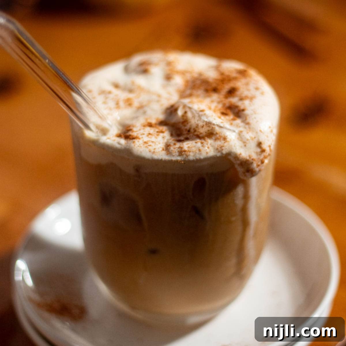 Starbucks Style Pumpkin Cold Foam 14 Glass of iced coffee with whipped pumpkin cold foam and a straw, sprinkled with pumpkin spice.