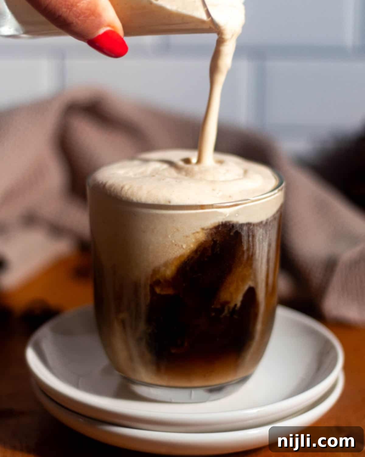 Starbucks Style Pumpkin Cold Foam 3 Pumpkin cold foam being poured over a glass of iced coffee with ice cubes visible.