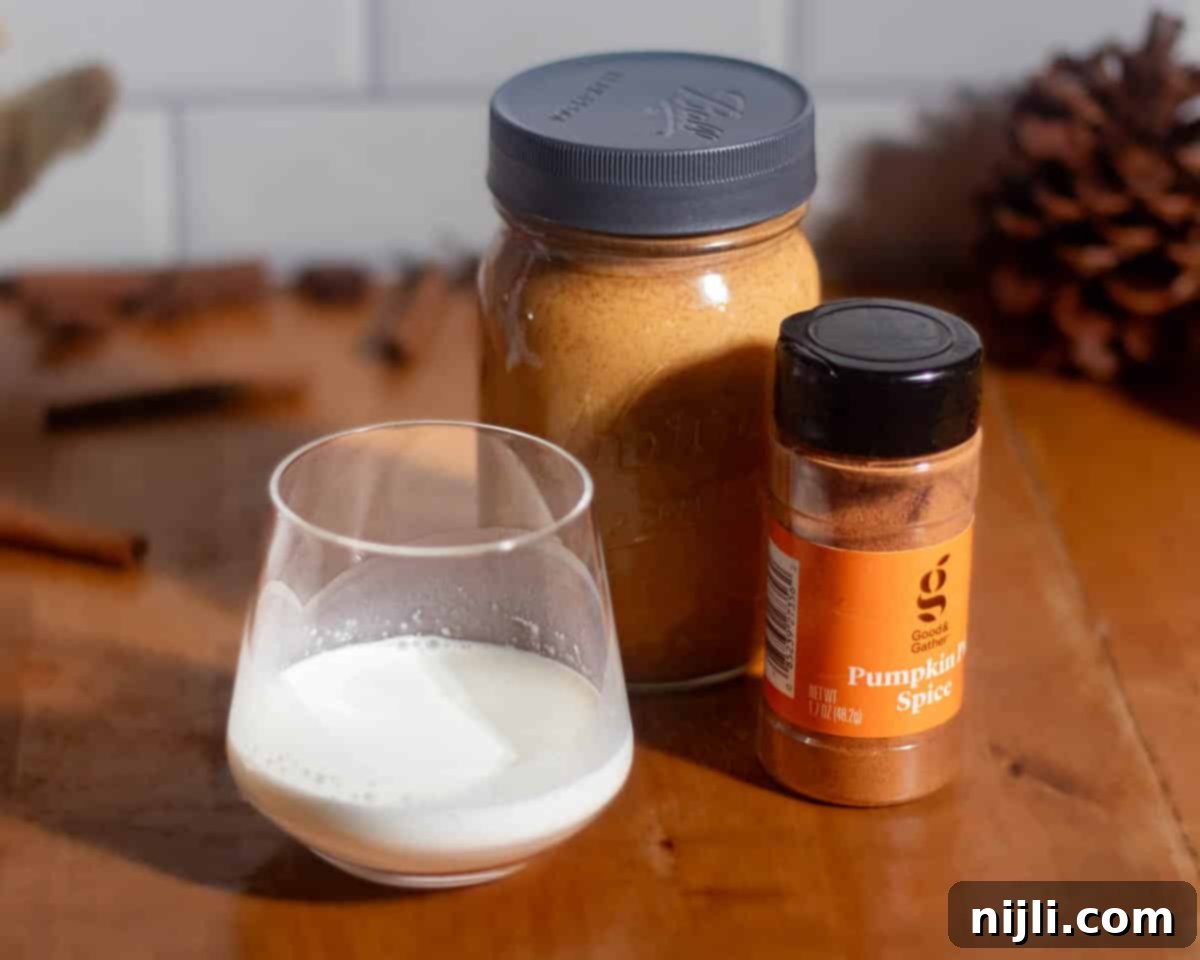 Starbucks Style Pumpkin Cold Foam 4 Ingredients for pumpkin cold foam recipe on a wooden table including pumpkin sauce in a mason jar, pumpkin pie spice, and half-and-half in a glass.