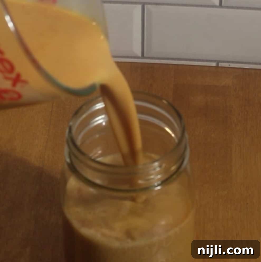 Starbucks Style Pumpkin Cold Foam 9 umpkin syrup mixture being poured into a mason jar for homemade pumpkin cold foam.