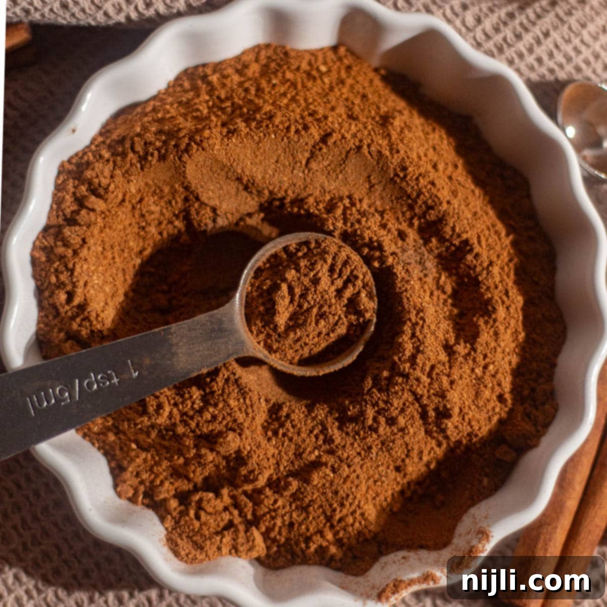 Spiced Pumpkin Harmony 2 Overhead view of homemade pumpkin spice blend in a white dish with a teaspoon scooping aromatic spices.
