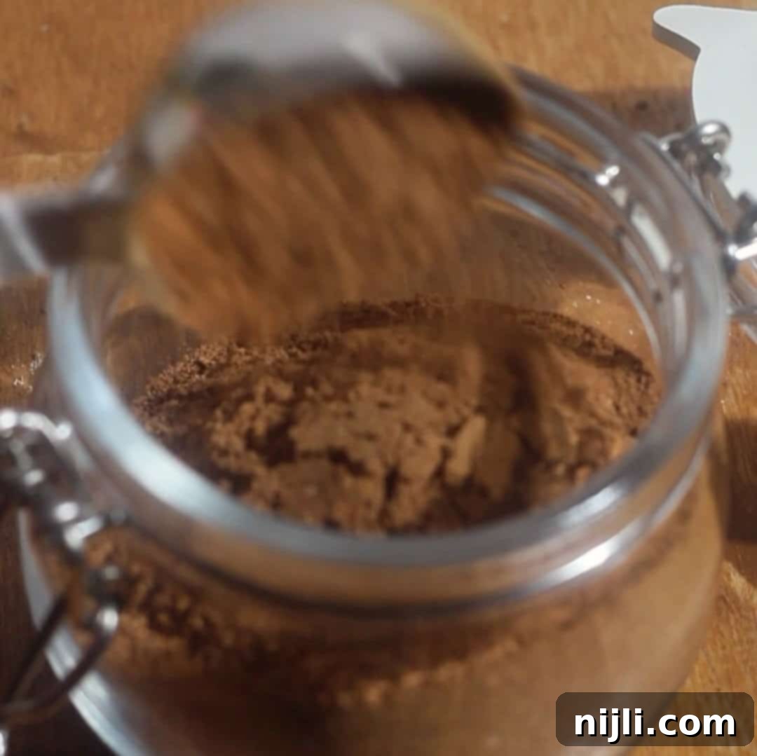 Spiced Pumpkin Harmony 9 Pumpkin spice blend being poured from a measuring spoon into a glass jar for airtight storage.