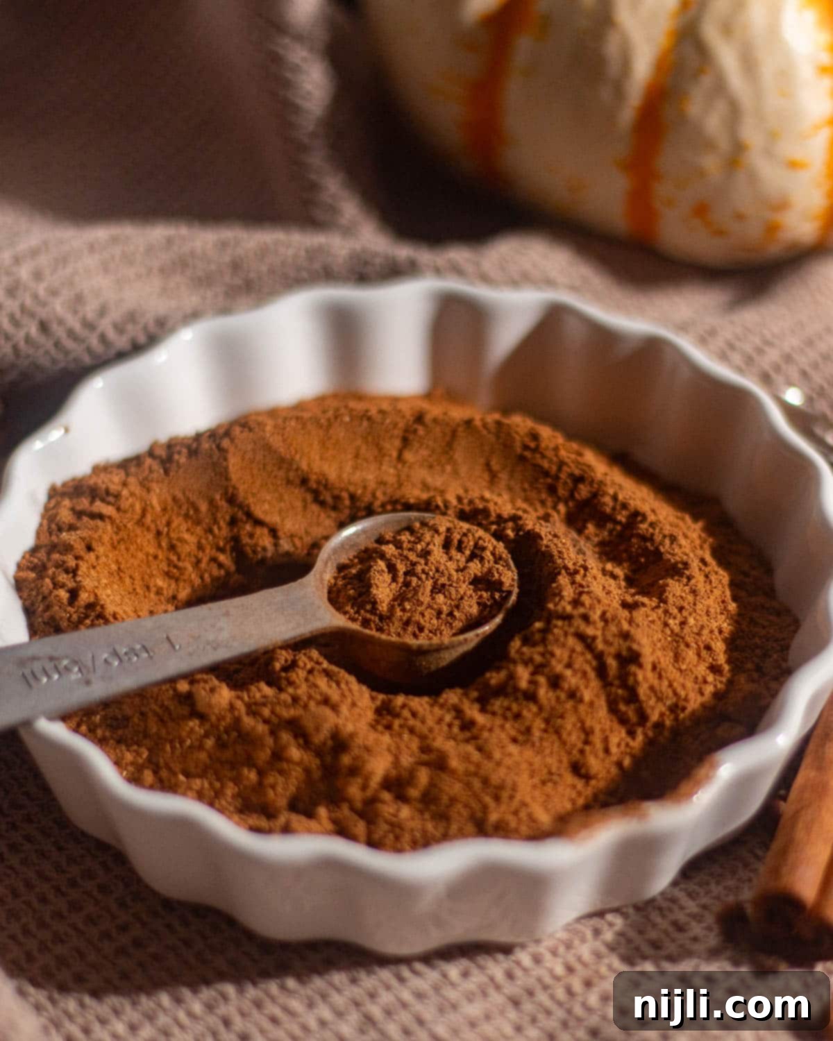 Spiced Pumpkin Harmony 10 White dish with ground pumpkin spice blend and a measuring spoon on top, ready for use.