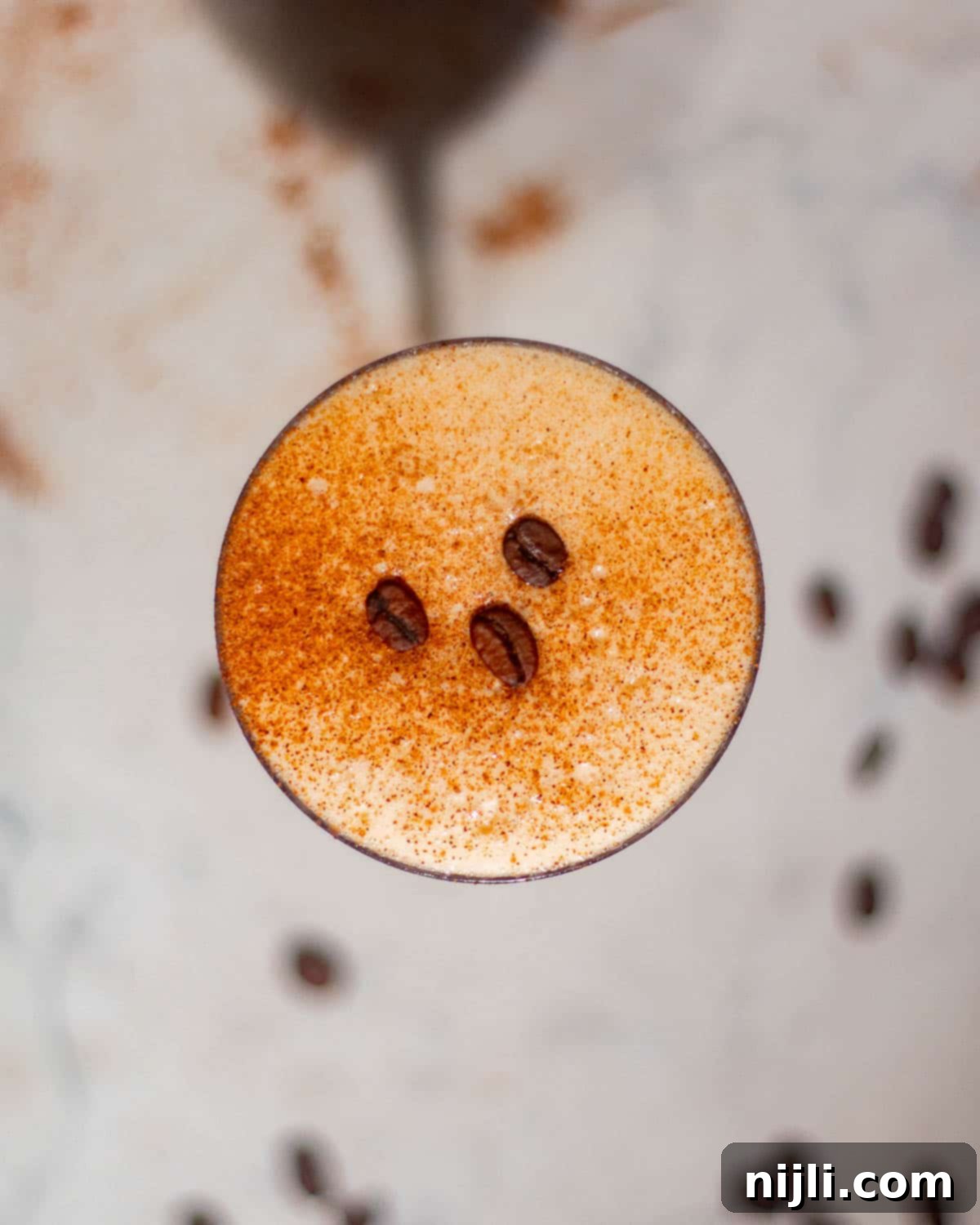 Overhead view of a rum espresso martini with frothy crema dusted with cinnamon and topped with coffee beans.
