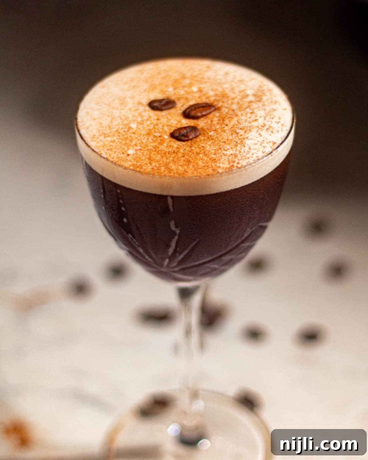 Elegant rum espresso martini in a coupe glass with coffee beans scattered around on the table.