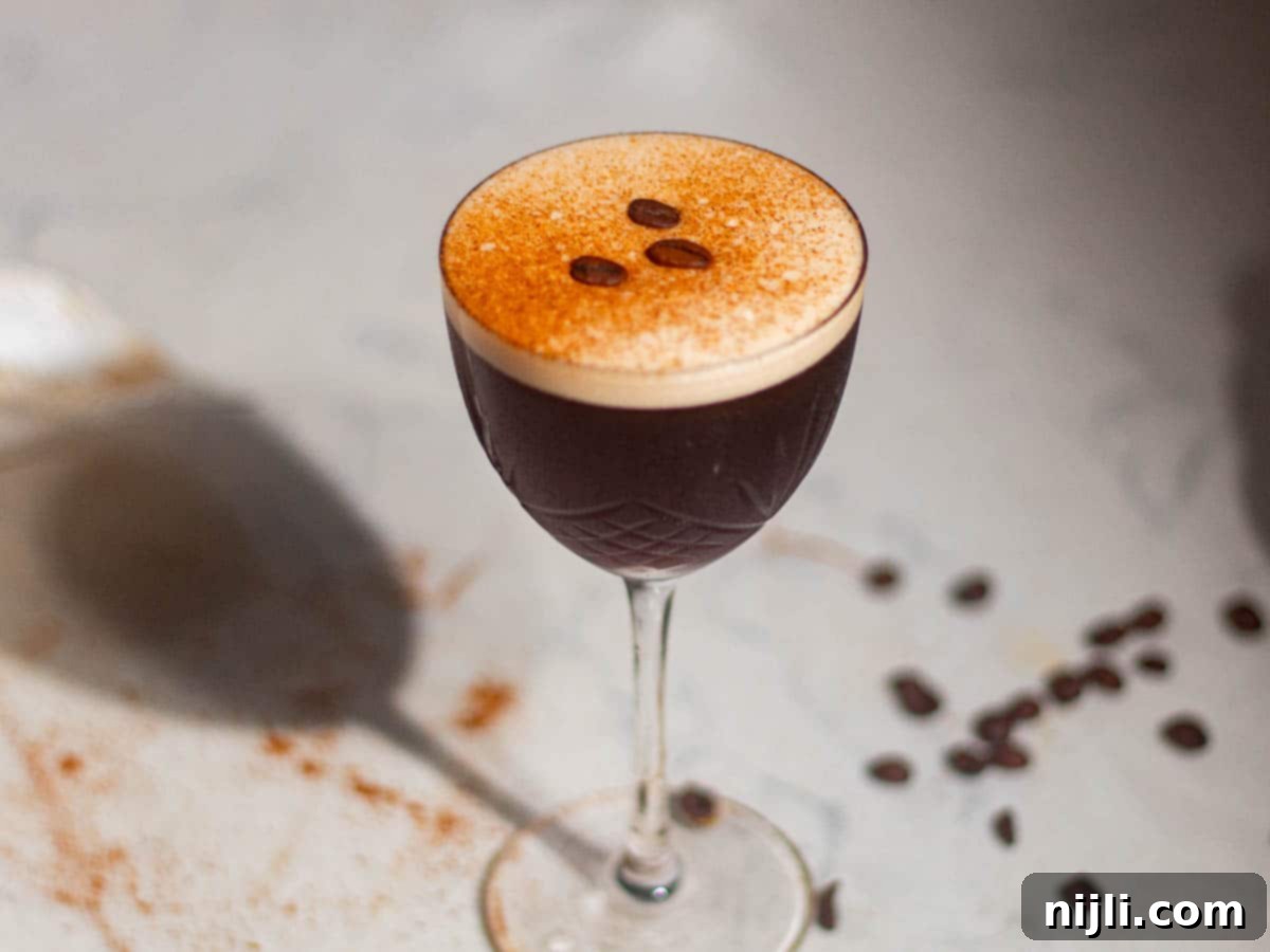 Elegant rum espresso martini in a coupe glass with coffee beans scattered around on the table.