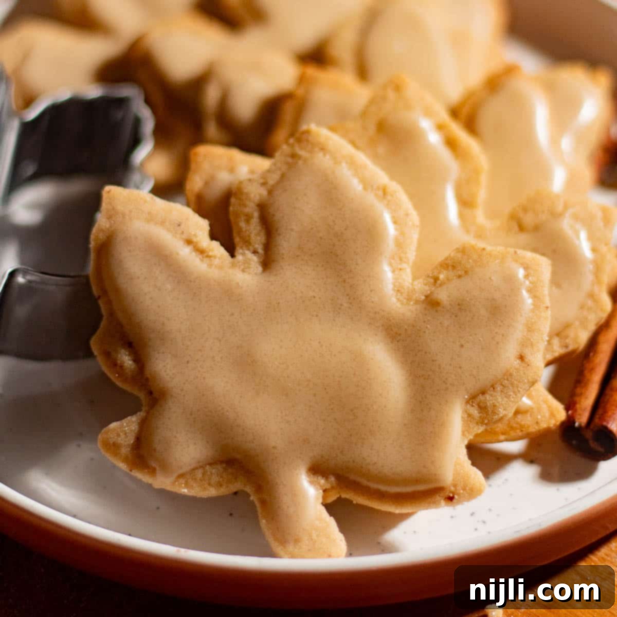 Plate of decorated brown butter cutout cookies with icing next to cinnamon sticks.