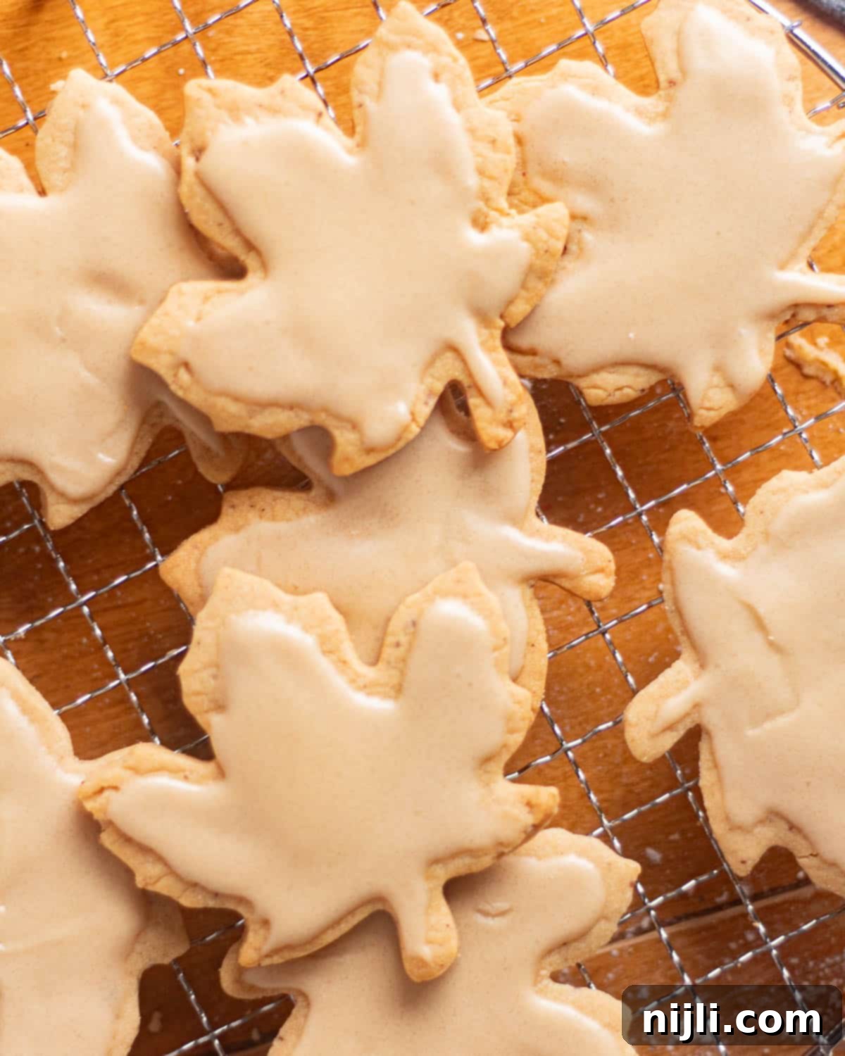 Brown Butter Bliss Cookies 13 Maple leaf cutout brown butter sugar cookies cooling on a wire rack with icing set on top.