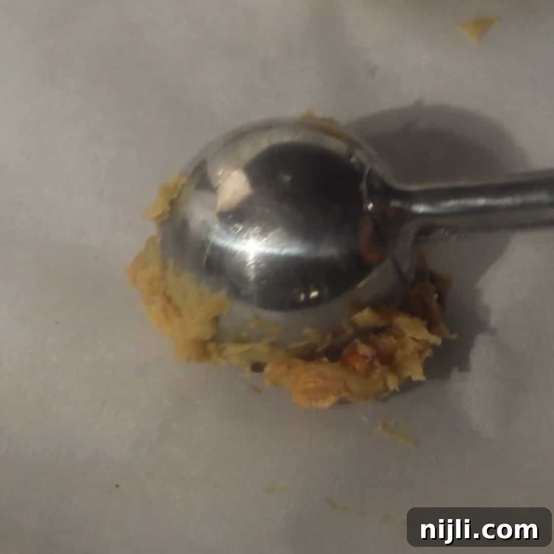 The Everything Cookie 11 Cookie scoop dropping chewy kitchen sink cookie dough onto a parchment-lined baking sheet.