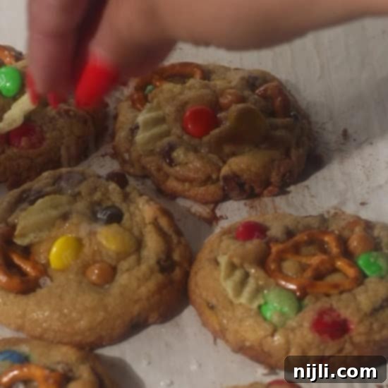 The Everything Cookie 12 Hand sprinkling sea salt over freshly baked kitchen sink cookies topped with pretzels, M&Ms, potato chips, and chocolate chips.