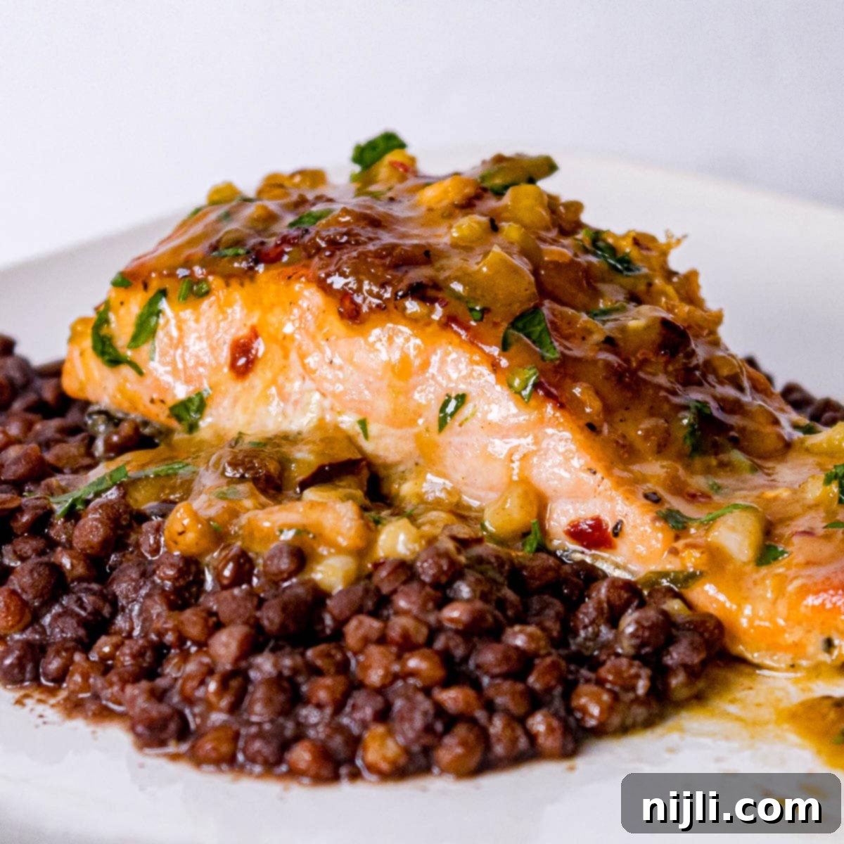 Maple Dijon Salmon 2 Crispy pan-seared maple dijon salmon on a plate, garnished with fresh herbs and served alongside a bed of lentils for a healthy, vibrant meal.