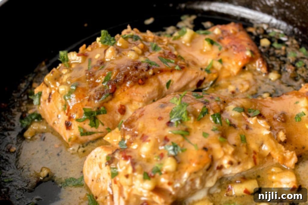 Maple Dijon Salmon 3 Close-up of perfectly cooked Maple Dijon Salmon in a cast iron skillet, generously coated with the glistening, flavorful sauce.