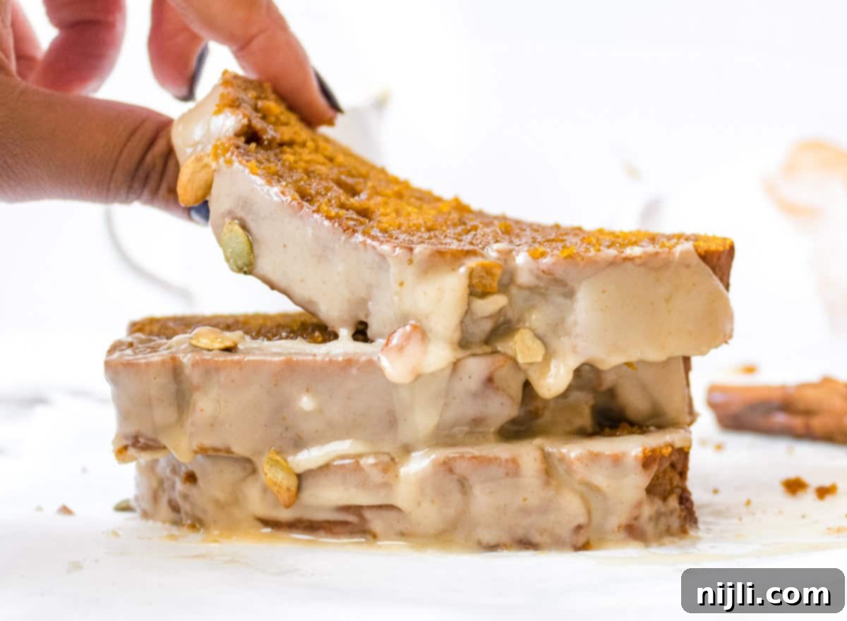 a hand picking up a slice of sour cream pumpkin bread from a stack