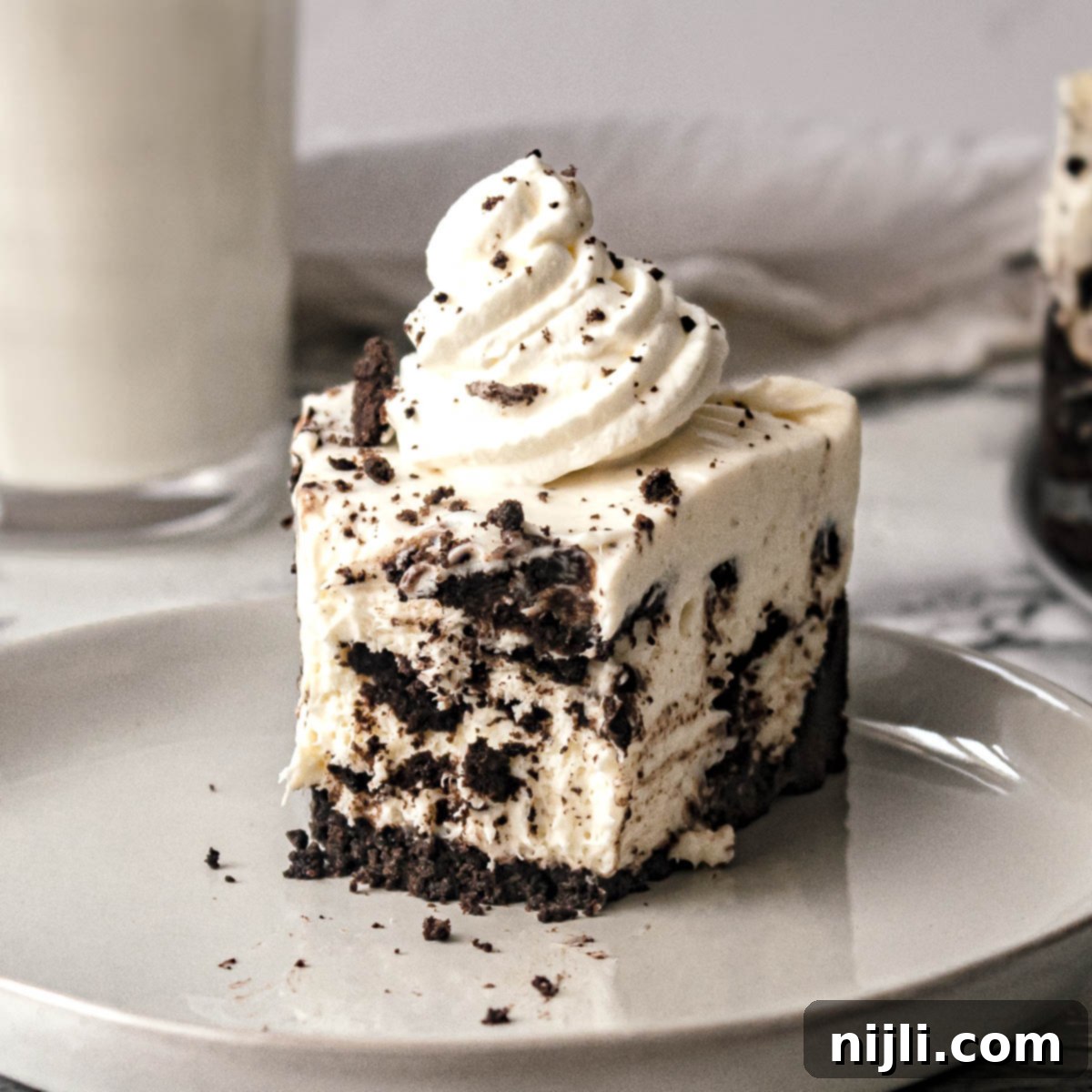 Decadent No-Bake Oreo Cheesecake 2 A slice of easy no bake oreo cheesecake on a plate topped with whipped cream, with a bite cut out.