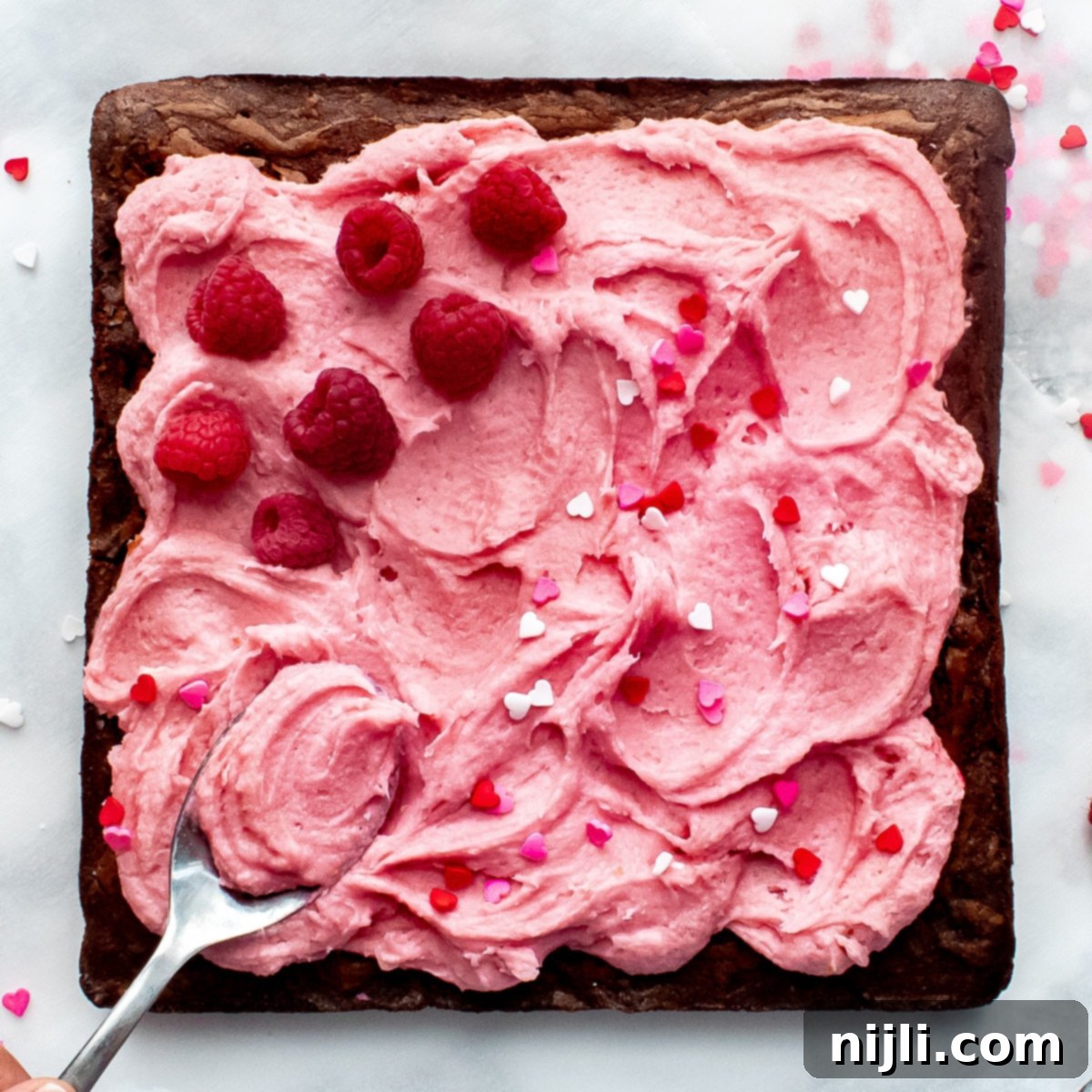 Fudgy Raspberry Chocolate Brownies 8 A spoon spreading frosting on raspberry chocolate brownies with fresh raspberries and sprinkles