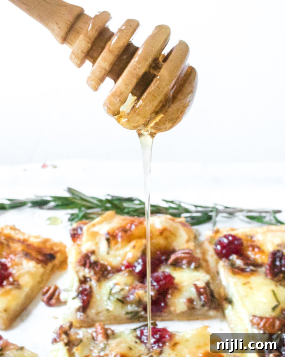 Vibrant Cranberry and Creamy Brie Tart 5 honey dipper drizzling honey over brie tart