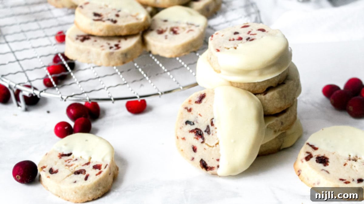 Cranberry White Chocolate Shortbread Delights 3 Stack of white chocolate cranberry shortbread cookies with more on a wire rack in the background.