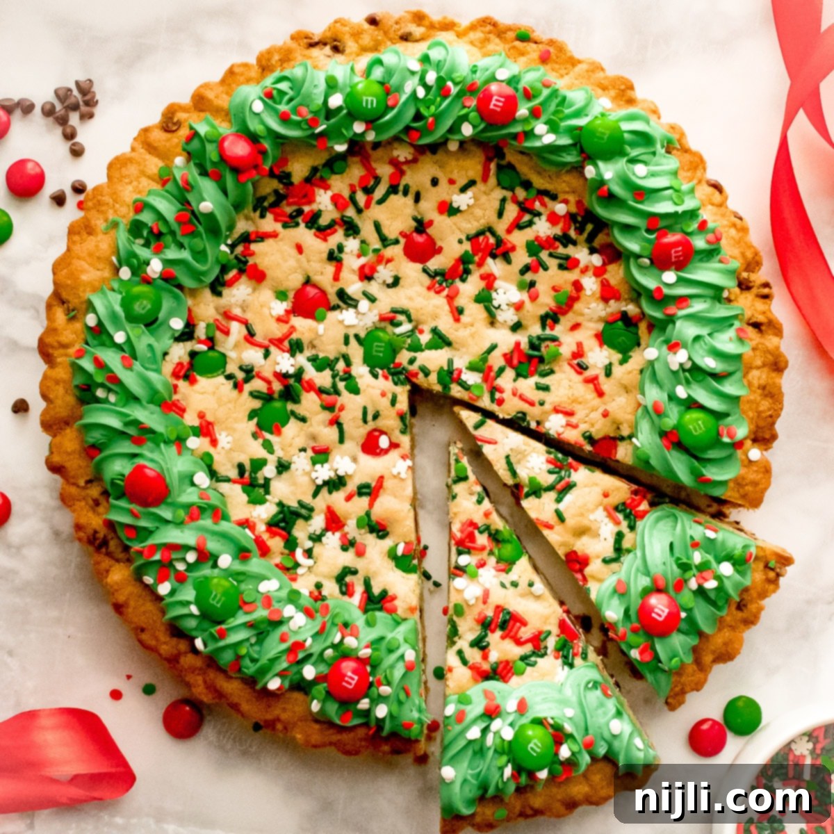 Festive Christmas Cookie Cake 8 Overhead shot of a festive Christmas Cookie cake with two slices cut, decorated with green frosting, M&M's, and sprinkles.