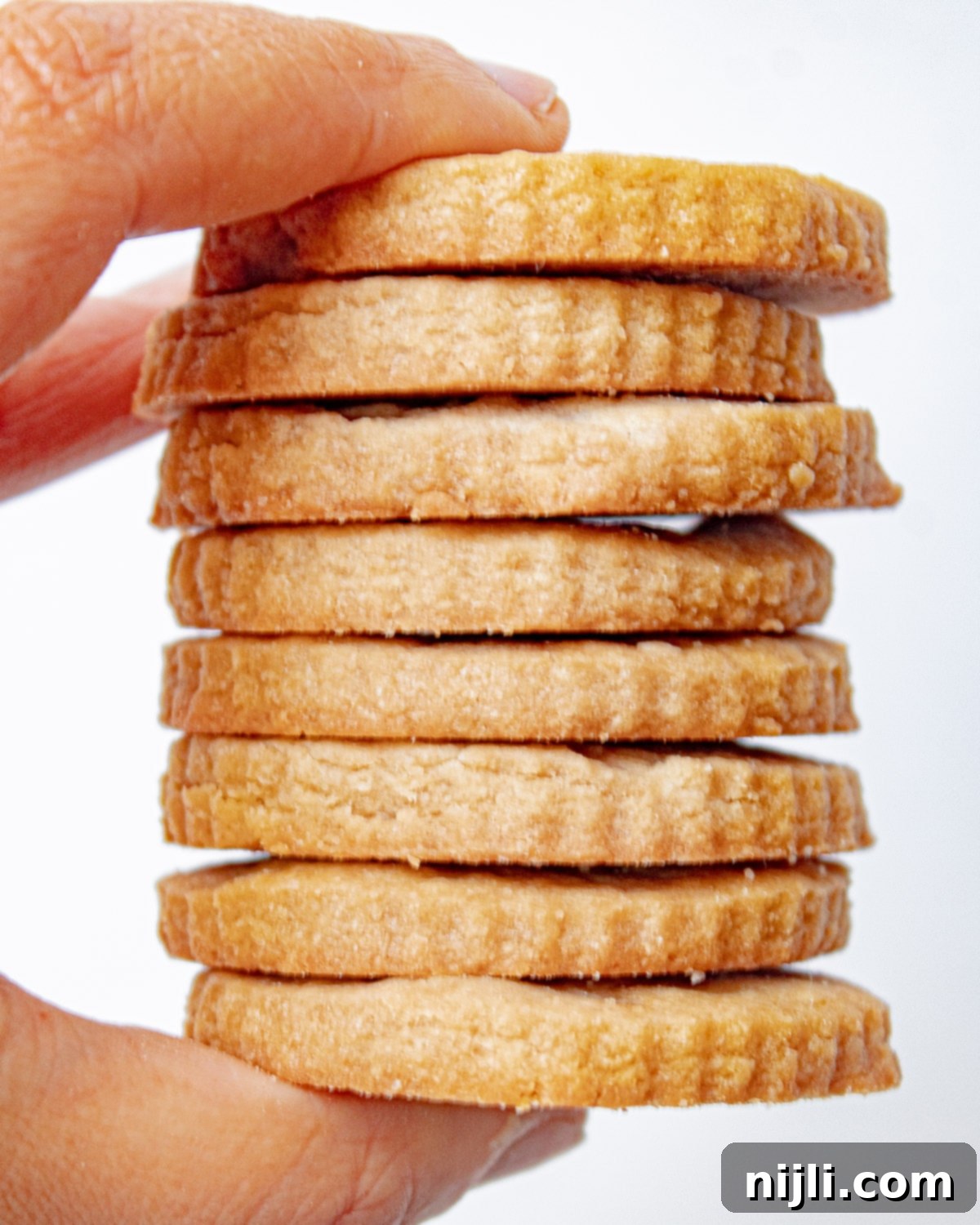 a hand holding a stack of brown sugar shortbread cookies