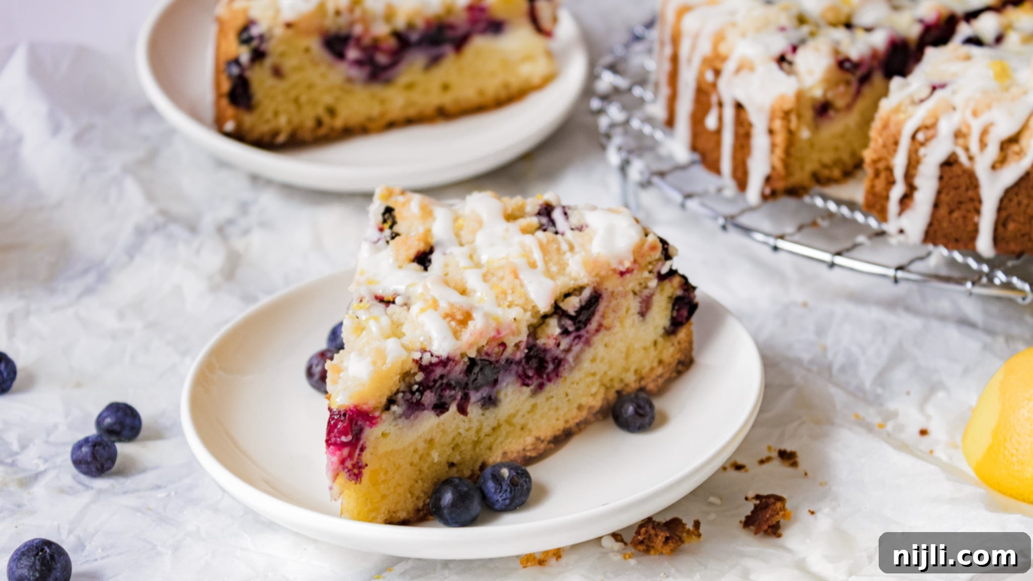 a slice of blueberry cream cheese coffee cake on a plate with the rest of the cake behind it