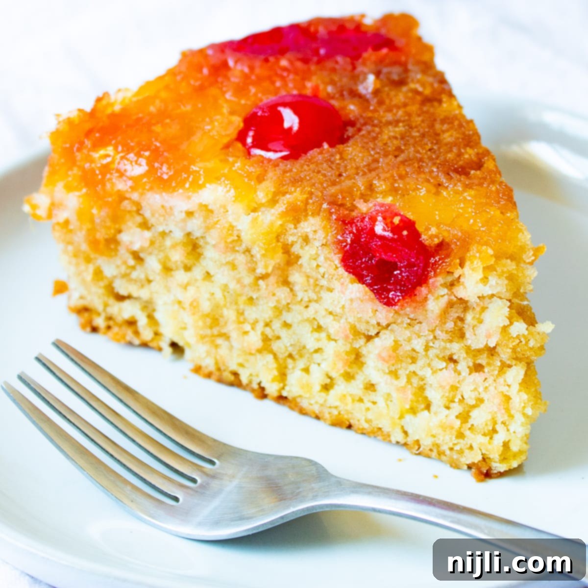 Closeup of vegan pineapple upside down cake slice with caramelized pineapple and cherry