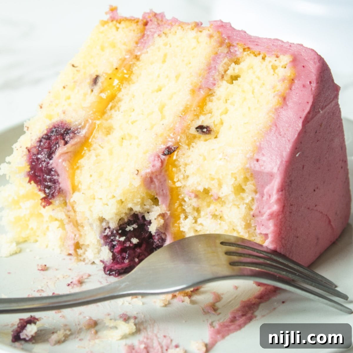 Sunshine Lemon Blackberry Delight 9 A delicious slice of lemon and blackberry cake on a plate with a couple bites taken out, highlighting its rich layers and appealing texture.