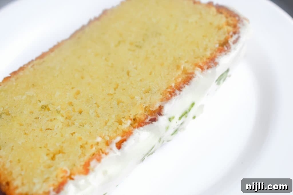 Slice of Key Lime Pound Cake on a white plate, topped with a generous amount of key lime glaze and zest.