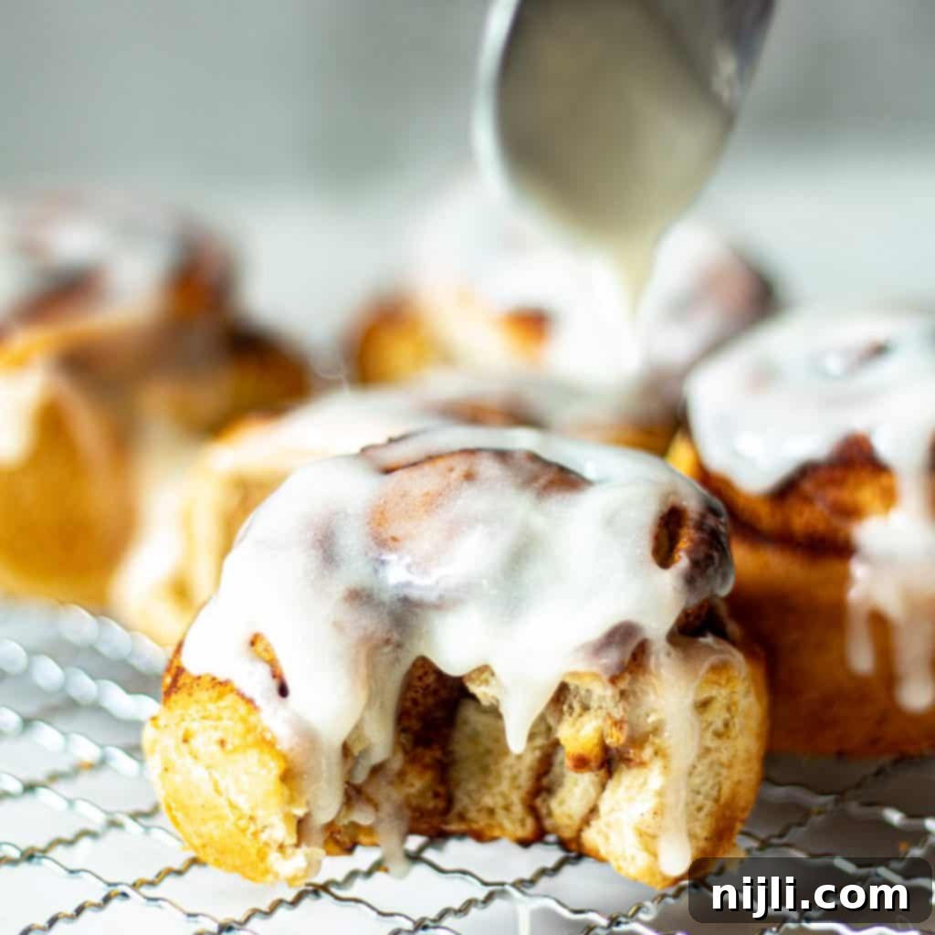 Air-Fried Cinnamon Rolls 4 Closeup of air fryer cinnamon rolls with icing, one with a bite taken out of it, showing soft interior