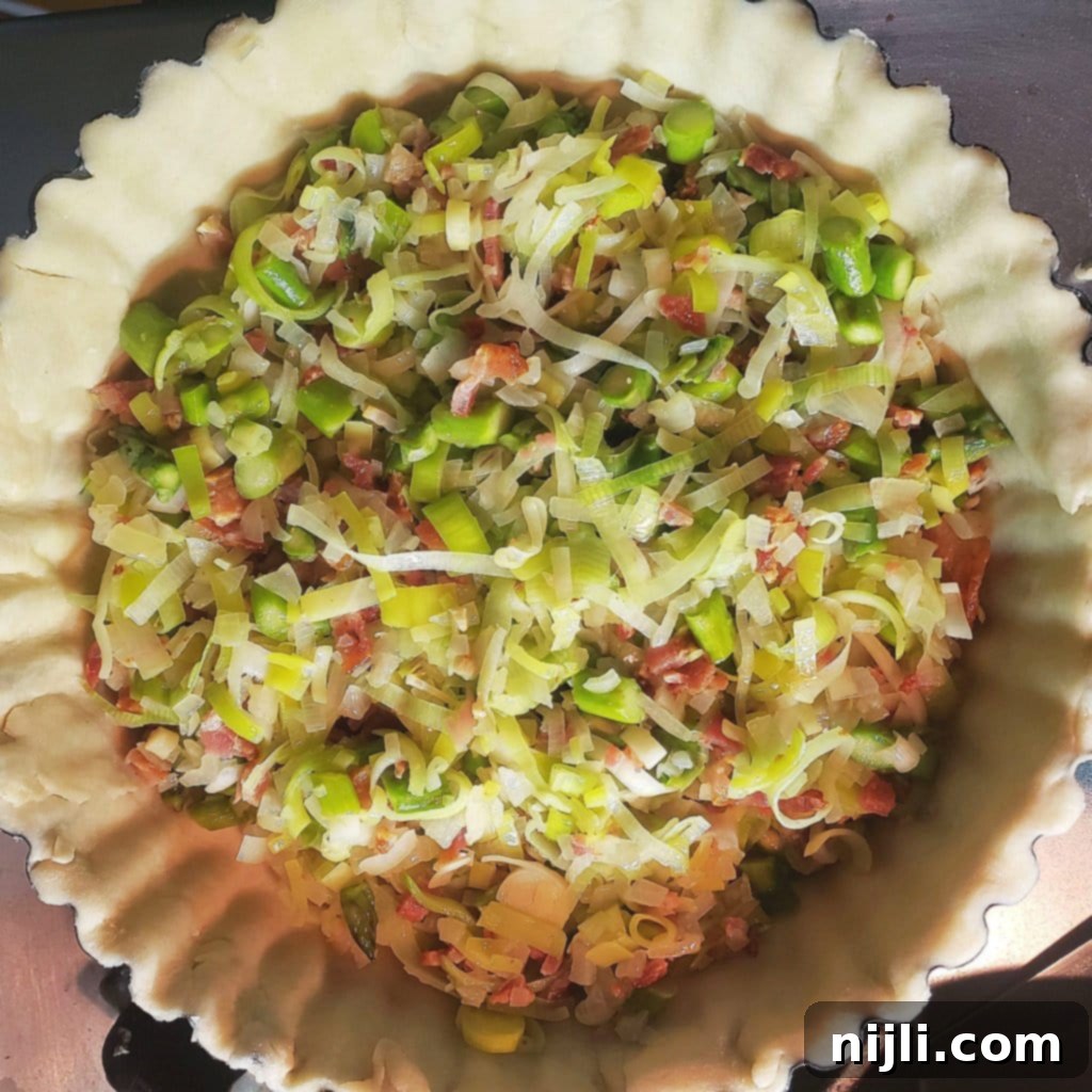 Decadent Bacon, Gruyère, Leek and Asparagus Quiche 9 Layering cheese and thyme over bacon and vegetable mixture in quiche crust | Chenée Today