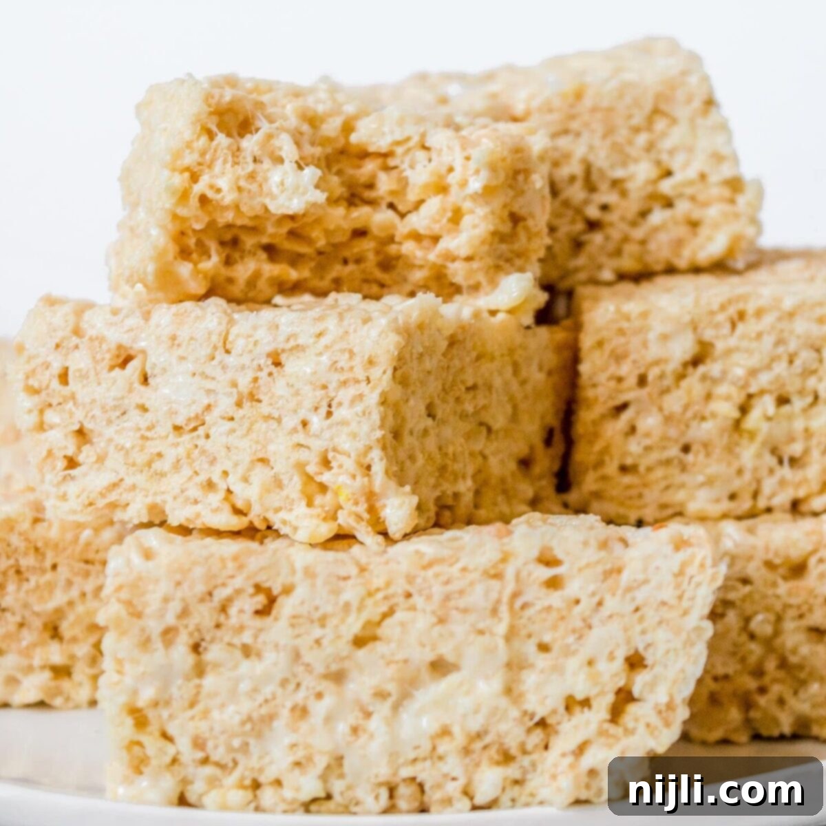 Gourmet Rice Krispie Treats with Brown Butter and White Chocolate Ganache 2 Stack of fancy Rice Krispie treats elegantly arranged on a white plate, showcasing their fluffy texture and uniform square cuts, perfect for high-tea or upscale dessert tables.