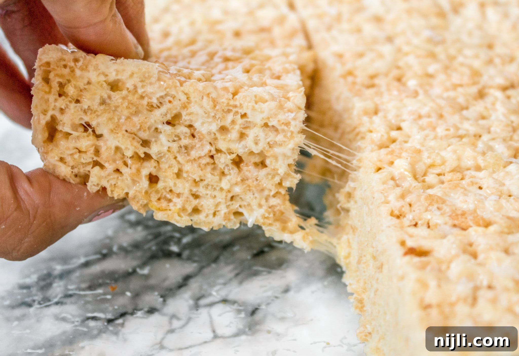 Gourmet Rice Krispie Treats with Brown Butter and White Chocolate Ganache 3 Close-up of a hand pulling apart a fancy Rice Krispie treat, showcasing the gooey marshmallow texture and airy crispness, perfect for a refined dessert experience.