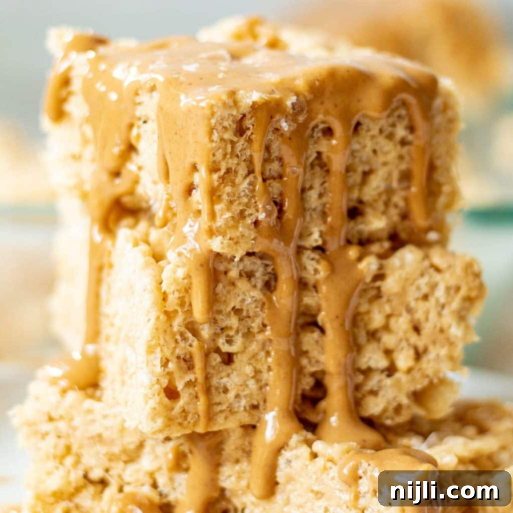 Peanut Butter Krispie Bars 2 Closeup of a stack of gooey peanut butter rice krispie treats with melted peanut butter drizzled on top, showcasing their irresistible texture.