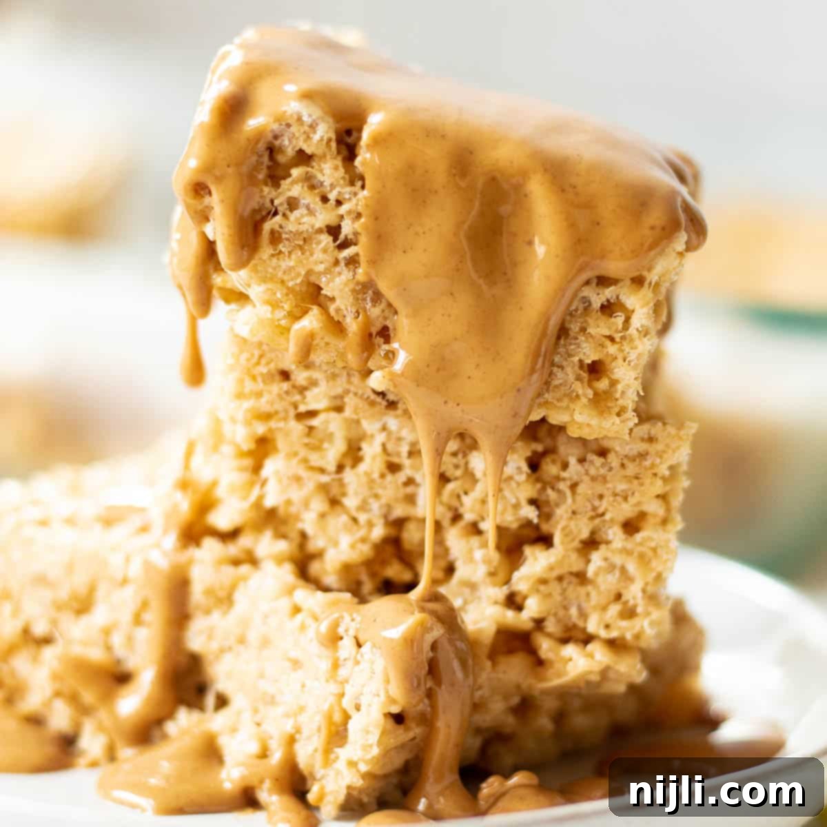 Peanut butter rice krispie treats drizzled with melted peanut butter, stacked neatly on a plate for serving.